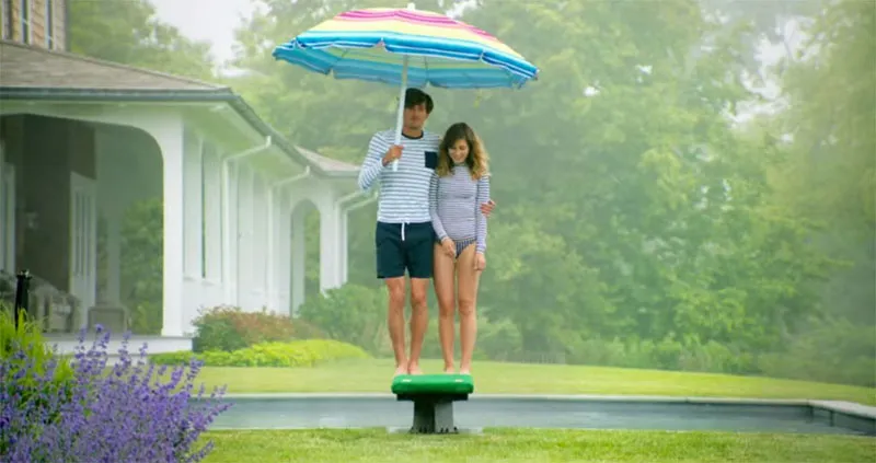 A photo of a man and woman standing on a diving board in the rain, the man is holding a colorful umbrella.